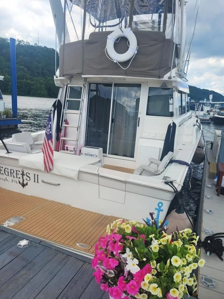 Slide: The Image of 1999 Silverton 37 Convertible yacht docked, featuring American flag and vibrant flowers. - 25