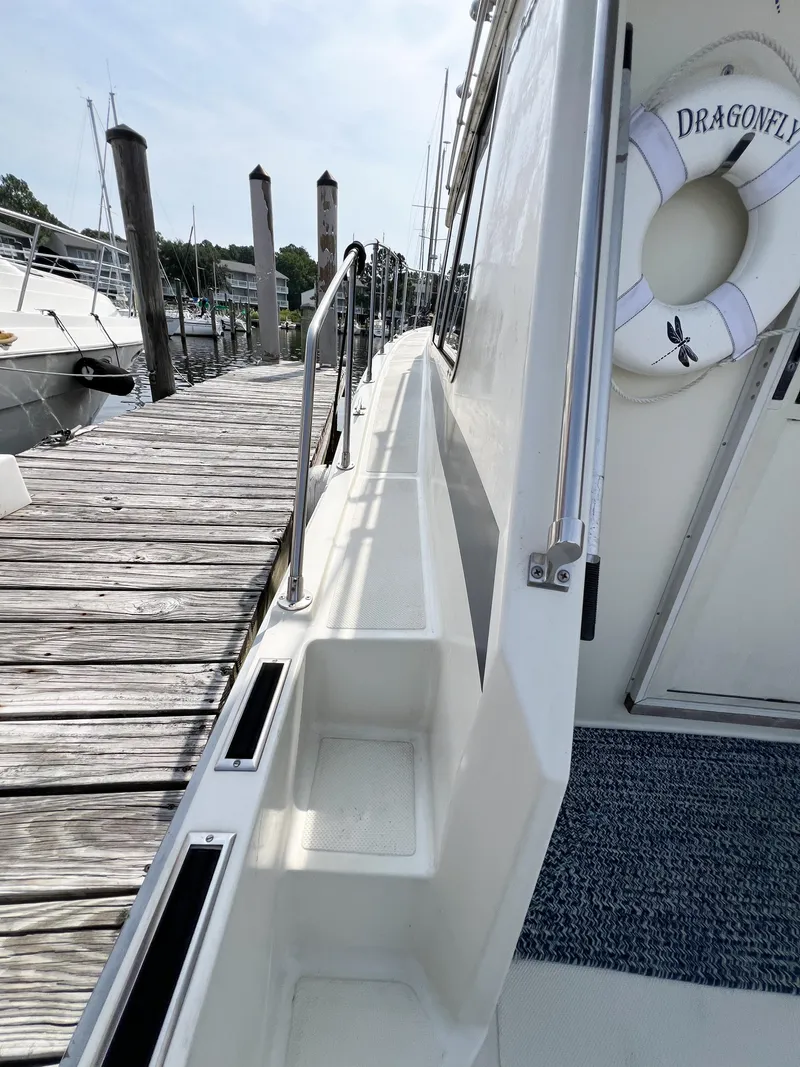 Slide: The Image of 1987 Tollycraft 34 Sport Sedan docked, featuring side deck and lifebuoy labeled "Dragonfly." - 16