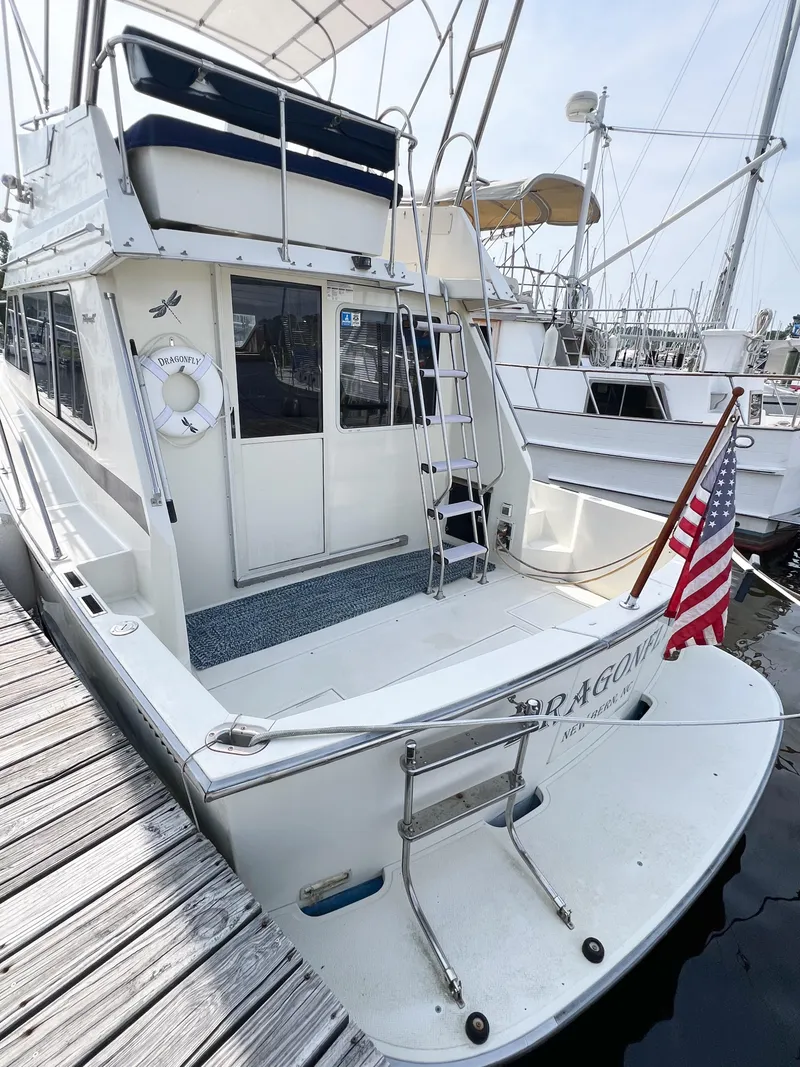 Slide: The Image of 1987 Tollycraft 34 Sport Sedan docked, featuring American flag and spacious deck area. - 9