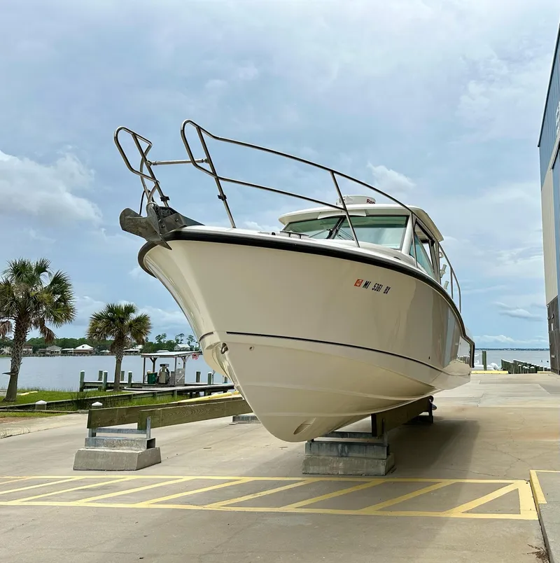 Slide: The Image of 2016 Boston Whaler 315 Conquest boat on dry dock, with palm trees and water in background. - 3