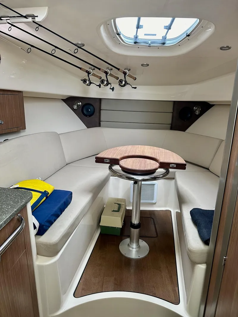 Slide: The Image of 2016 Boston Whaler 315 Conquest cabin interior with seating, table, and fishing rods. - 32