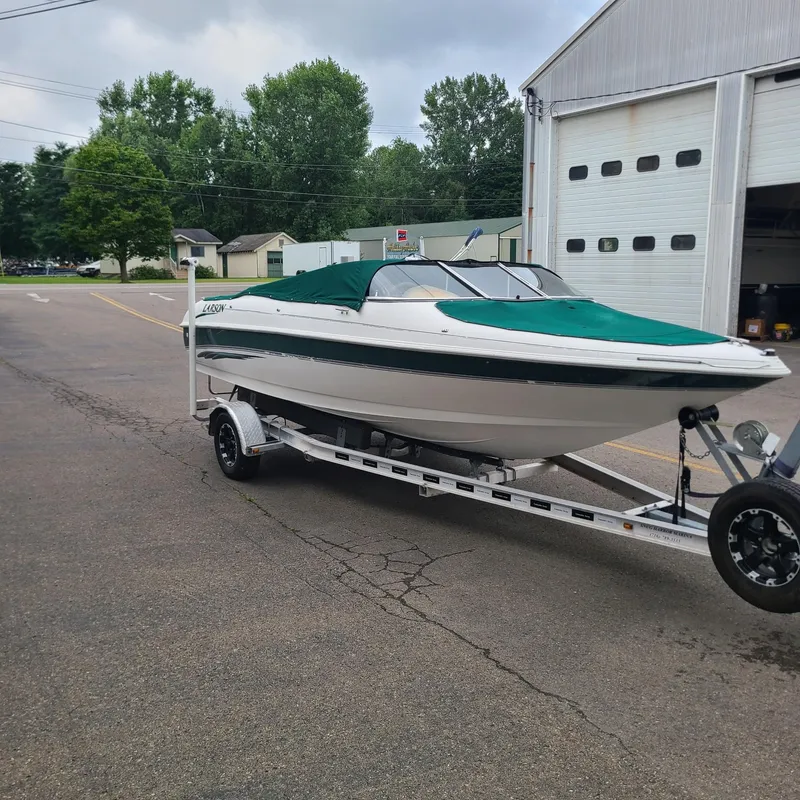Slide: The Image of 1999 Larson 206 boat on trailer outside garage, green cover, overcast day. - 3