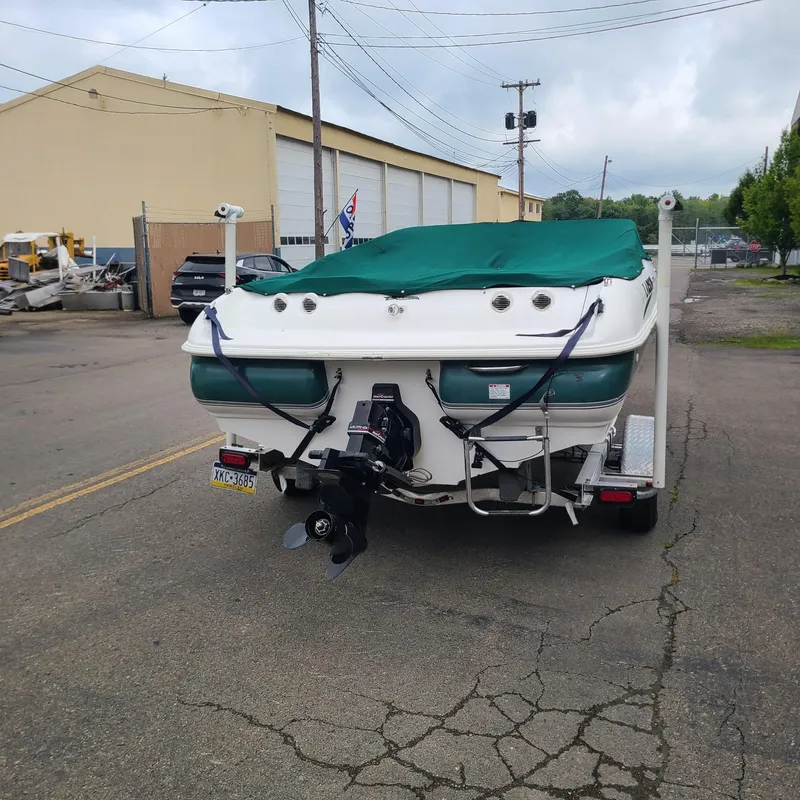Slide: The Image of 1999 Larson 206 boat on trailer with green cover, parked on street. - 4