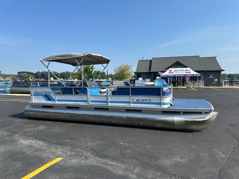 The Image of 1989 AquaPatio 24 pontoon boat parked in a marina lot under clear blue skies. - 0
