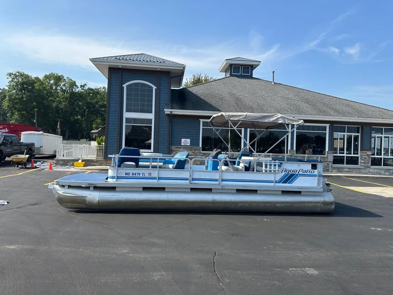 Slide: The Image of 1989 AquaPatio 24 pontoon boat parked outside a building on a sunny day. - 2