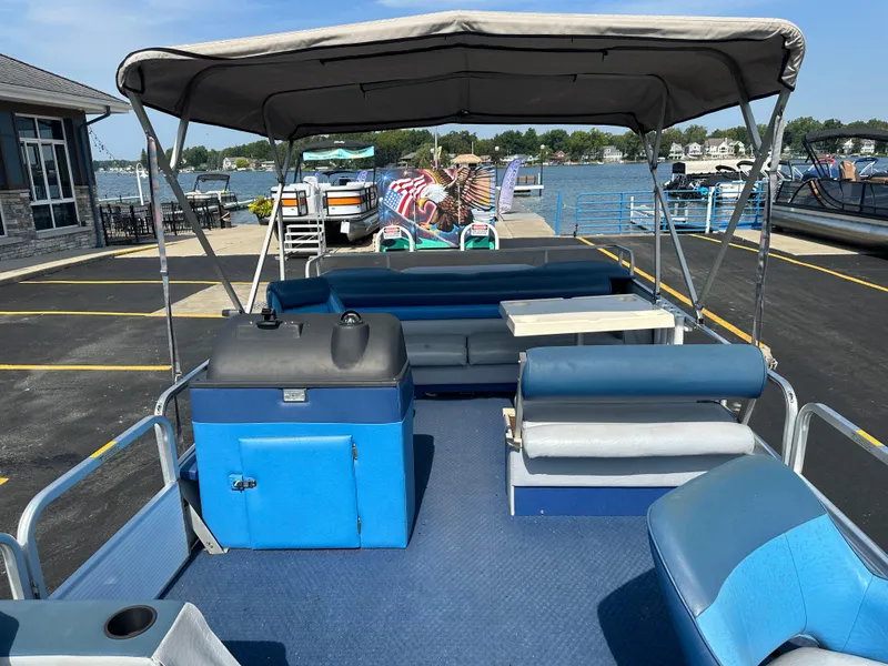 Slide: The Image of 1989 AquaPatio 24 pontoon boat with canopy, docked by a lake, featuring blue seating and storage. - 9