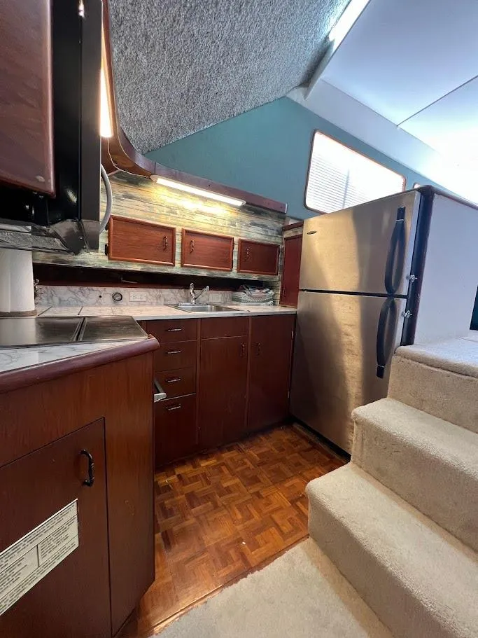 Slide: The Image of 1987 Ocean Yachts Super Sport kitchen with wood cabinets, stainless steel fridge, and carpeted stairs. - 7