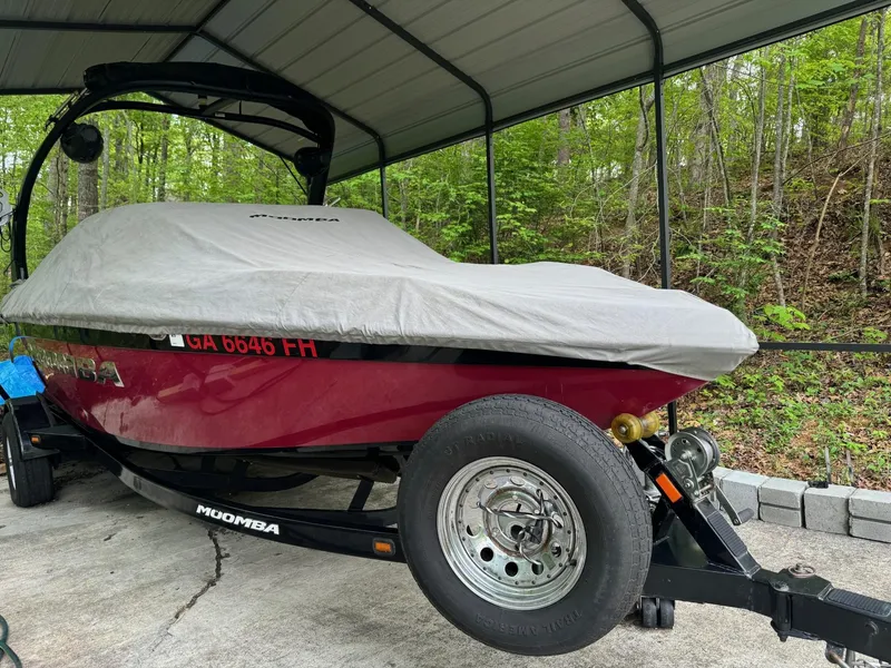 Slide: The Image of 2011 Moomba Mobius LSV boat covered, parked under a shelter in a wooded area. - 10