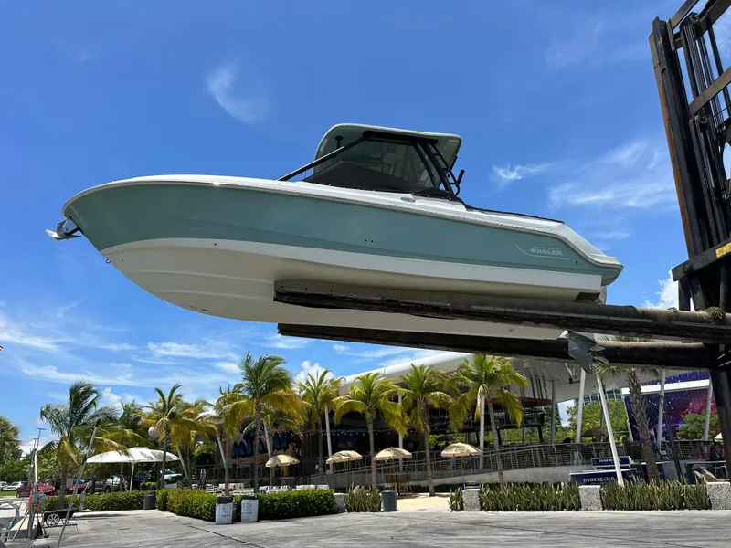 Slide: The Image of 2021 Boston Whaler 240 Vantage boat lifted, with palm trees and blue sky background. - 2