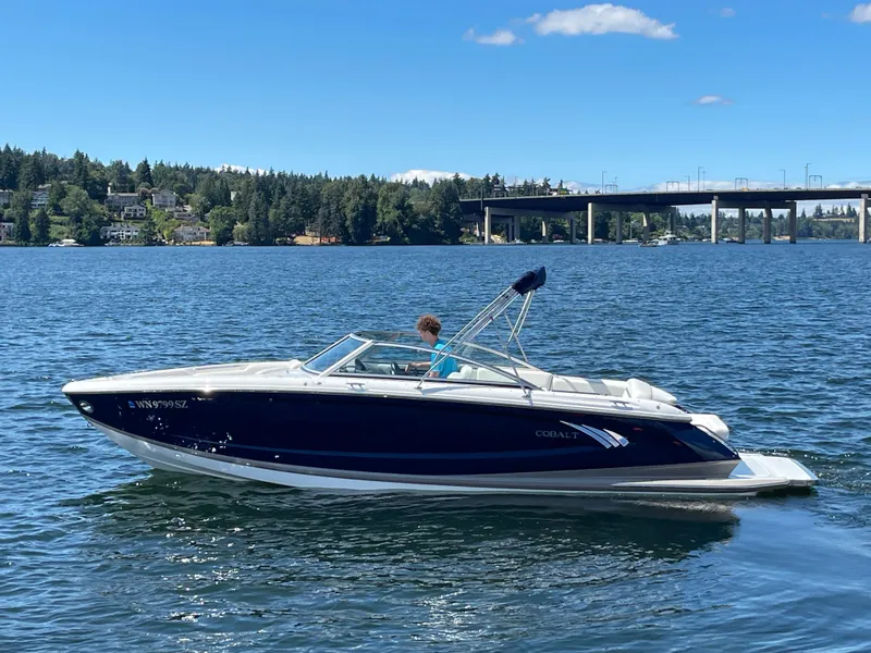 Slide: The Image of 2011 Cobalt A25 boat cruising on a sunny lake with a bridge in the background. - 1