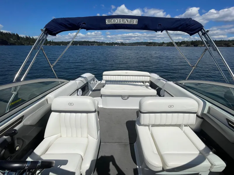 Slide: The Image of 2011 Cobalt A25 boat interior with white seating, blue canopy, on a calm lake. - 20