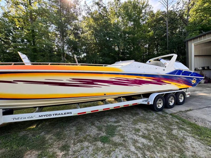 Slide: The Image of 1990 Fountain 42 Lightning speedboat with vibrant graphics on a trailer, surrounded by trees. - 1