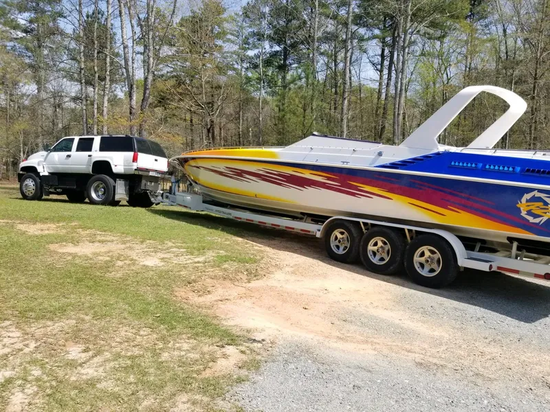 Slide: The Image of SUV towing a colorful 1990 Fountain 42 Lightning speedboat on a trailer in a wooded area. - 14