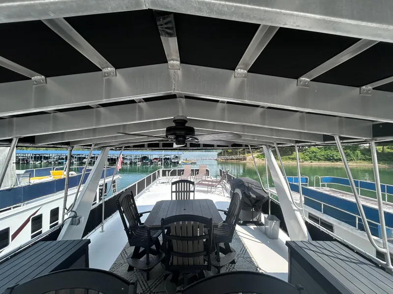 Slide: The Image of Majestic 2004 houseboat deck with seating, docked by a serene lake. - 9