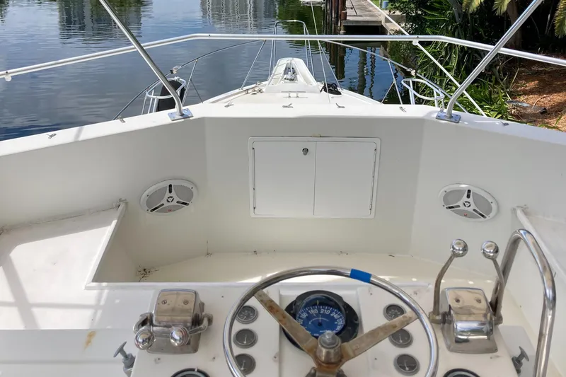 Slide: The Image of 1976 Hatteras 46 boat helm with steering wheel and controls, docked by calm water. - 11