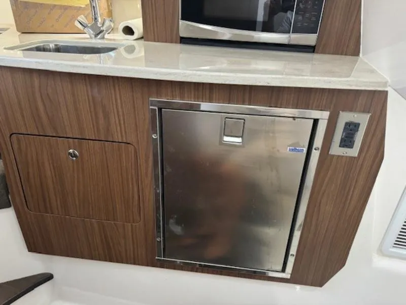 Slide: The Image of Compact kitchenette in 2016 Everglades 360LXC boat with sink, microwave, and stainless steel fridge. - 11