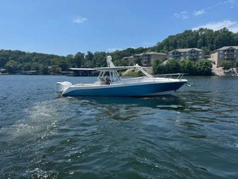 Slide: The Image of 2016 Everglades 360LXC boat cruising on a scenic lake with waterfront homes. - 24