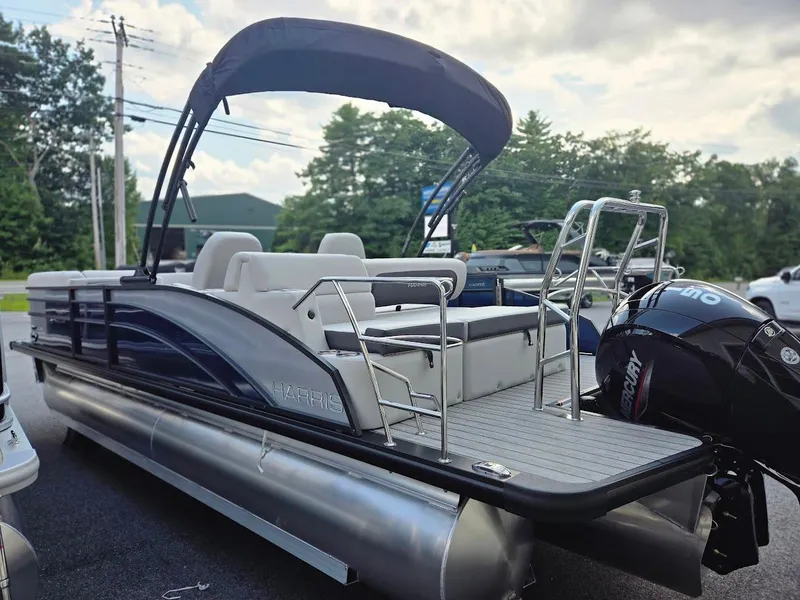 Slide: The Image of 2025 Harris Cruiser 230 pontoon boat with canopy and outboard motor, parked outdoors. - 7