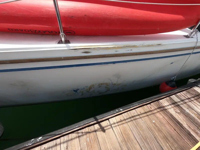Slide: The Image of 1985 Catalina 30 sailboat with visible hull wear, docked beside a wooden pier. - 2