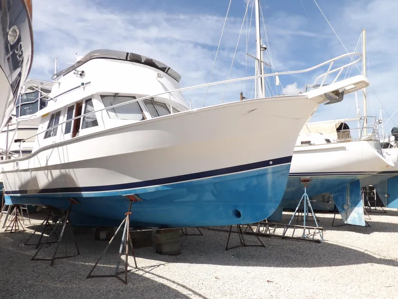 Slide: The Image of 1999 Mainship 350 Trawler on stands, white and blue hull, in boatyard. - 1