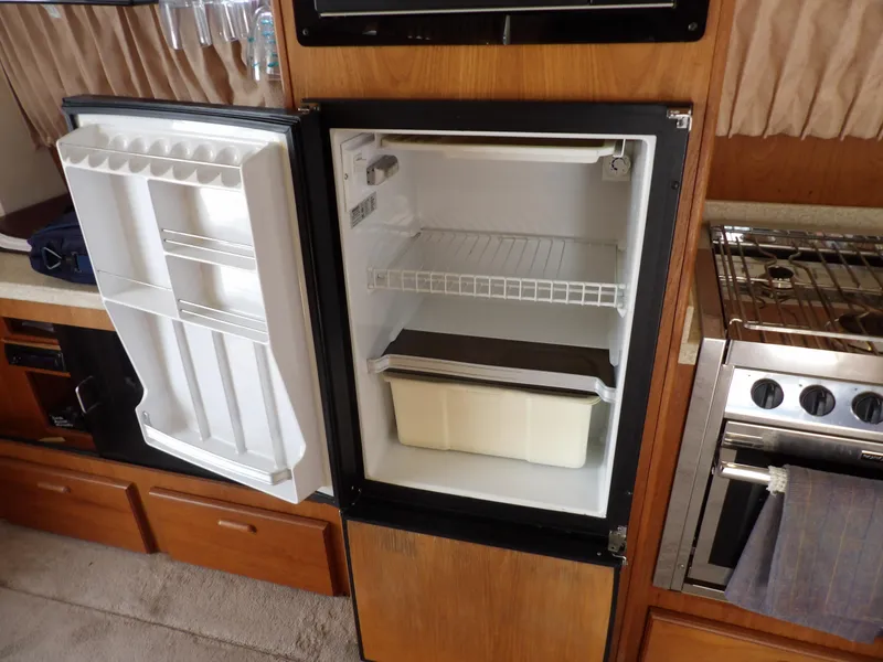 Slide: The Image of Open refrigerator in 1999 Mainship 350 Trawler kitchen, showing interior shelves and adjacent stove. - 38