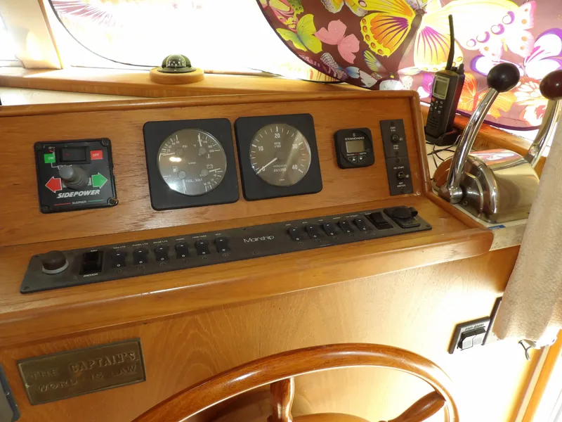 Slide: The Image of 1999 Mainship 350 Trawler helm with gauges, controls, and decorative butterfly curtain. - 44