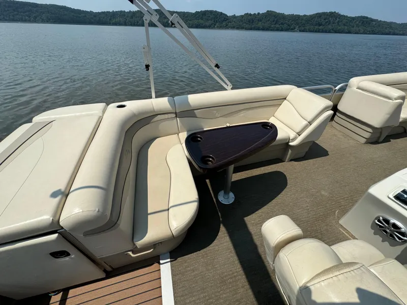Slide: The Image of 2014 Bennington 24 SLX3 pontoon boat with beige seating, table, and scenic lake view. - 9