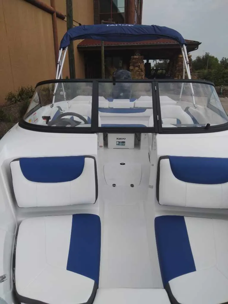 Slide: The Image of 2024 Tahoe 200 S boat with blue and white seating, docked near a building. - 2