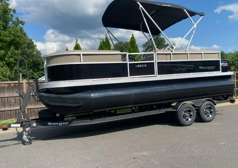 Slide: The Image of 2024 Ranger Reata 200C pontoon boat on trailer, parked outdoors under blue sky. - 2