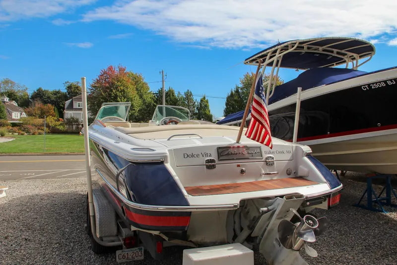 Slide: The Image of 2004 Chris-Craft Launch 25 boat with American flag, parked on gravel. - 35