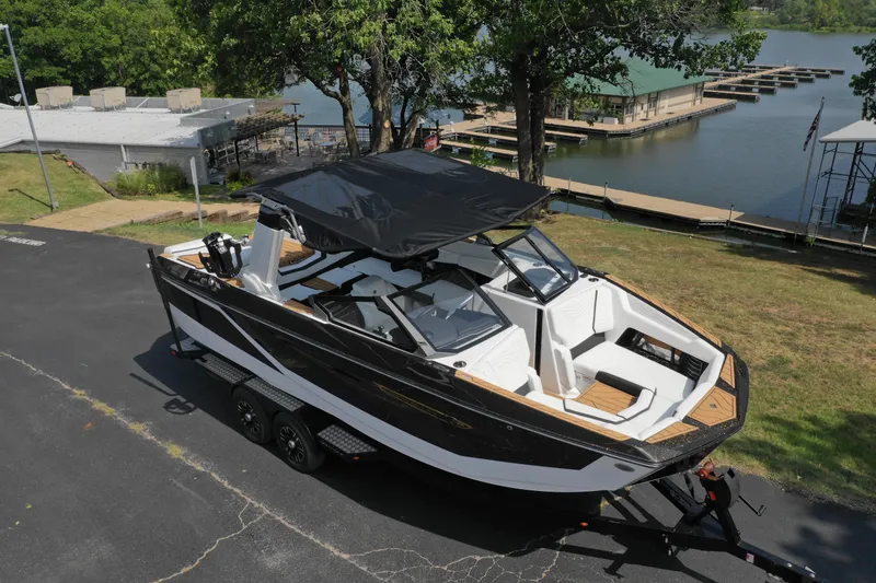 Slide: The Image of 2025 Nautique G23 boat on trailer near a lakeside dock. - 13