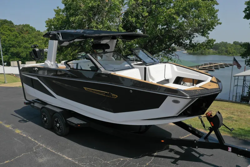 Slide: The Image of 2025 Nautique G23 boat on trailer by a lake, surrounded by trees. - 3