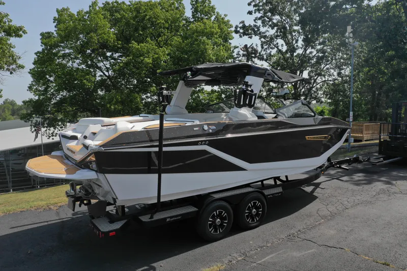 Slide: The Image of 2025 Nautique G23 boat on trailer, parked outdoors, surrounded by trees. - 4
