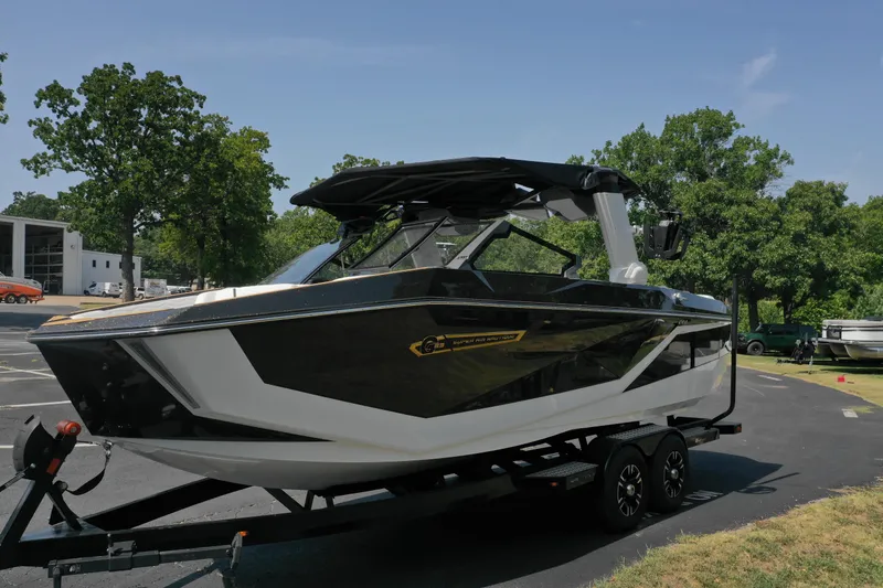 Slide: The Image of 2025 Nautique G23 boat on trailer, parked outdoors, surrounded by trees. - 5