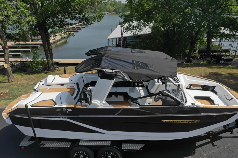 Slide: The Image of 2025 Nautique G23 boat with black canopy, parked near a scenic lake. - 9