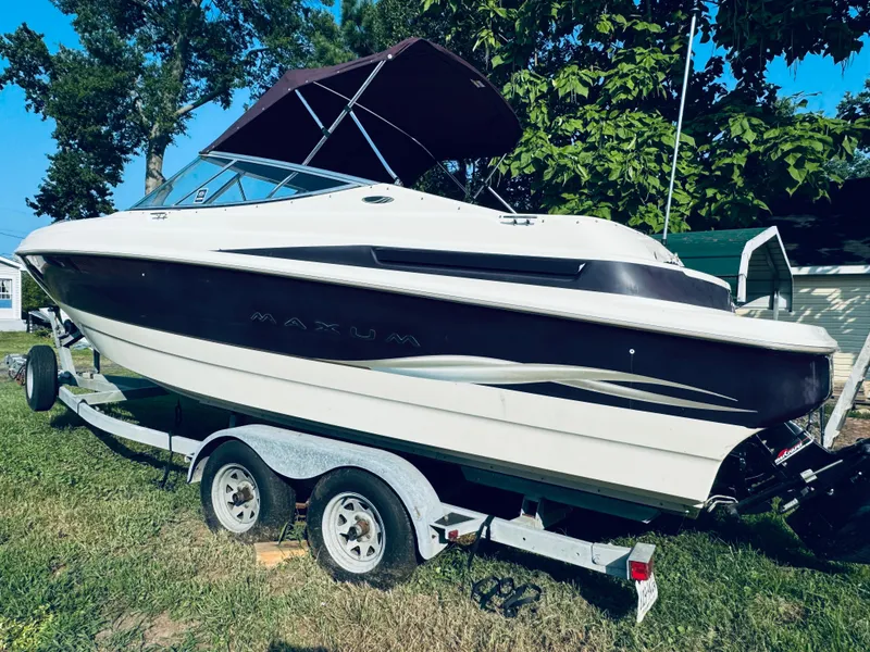 Slide: The Image of 1999 Maxum 230 boat on trailer, parked on grass with trees in background. - 0