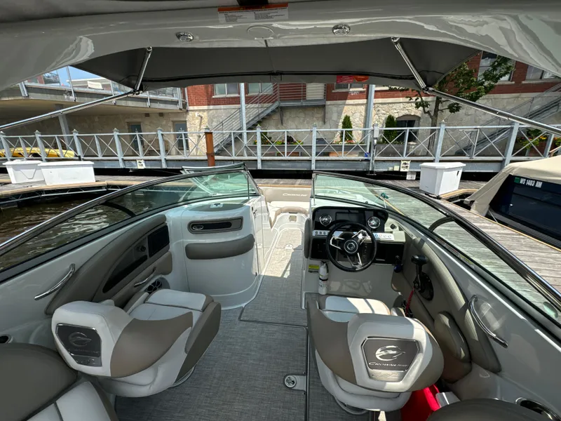 Slide: The Image of 2023 Crownline 255 XS boat interior with modern seating and dashboard at a dock. - 12