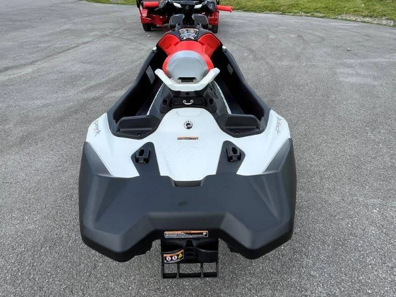 Slide: The Image of 2024 Sea-Doo Spark Trixx jet ski, rear view, red and white design on pavement. - 13