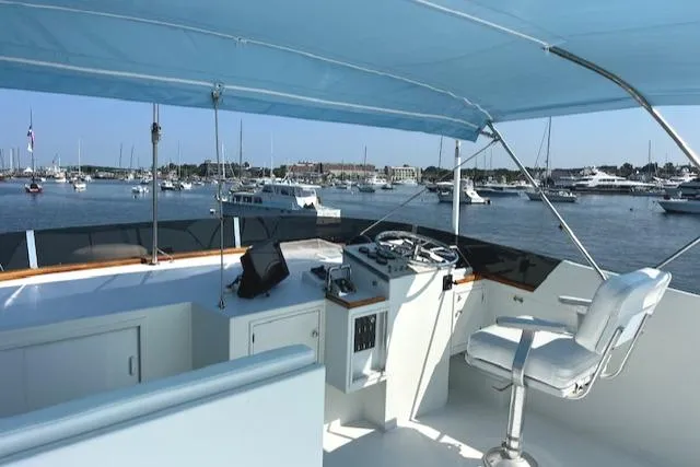 Slide: The Image of 1980 Huckins Sports Cruiser helm with marina view, featuring blue canopy and white seating. - 13