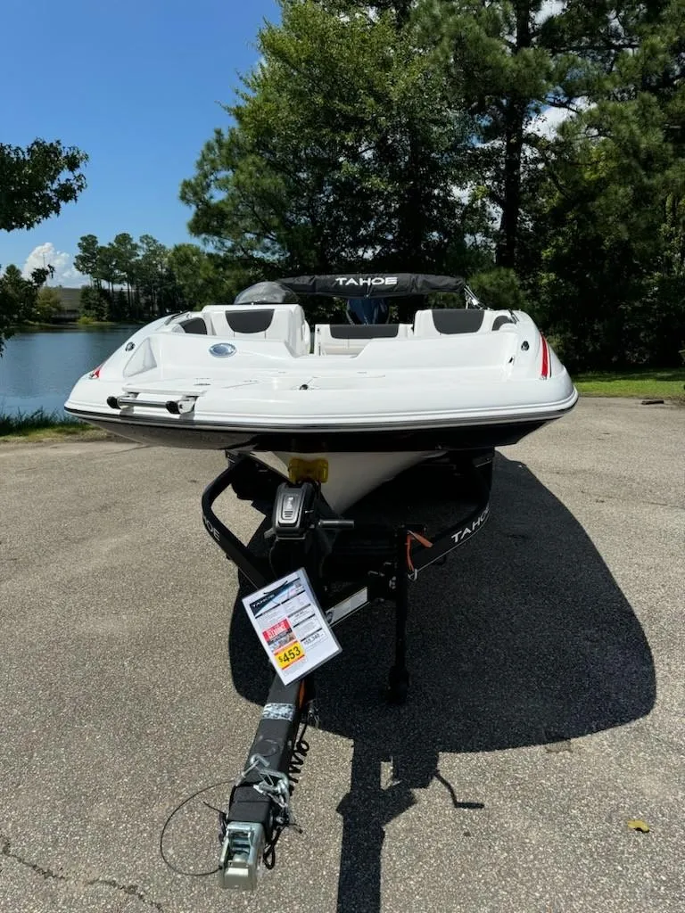Slide: The Image of 2024 Tahoe 2150 boat on trailer, parked outdoors near trees and water. - 2