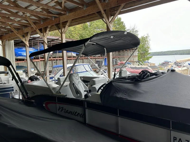 Slide: The Image of 2022 Manitou Encore 25 pontoon boat in covered storage by a lake. - 20