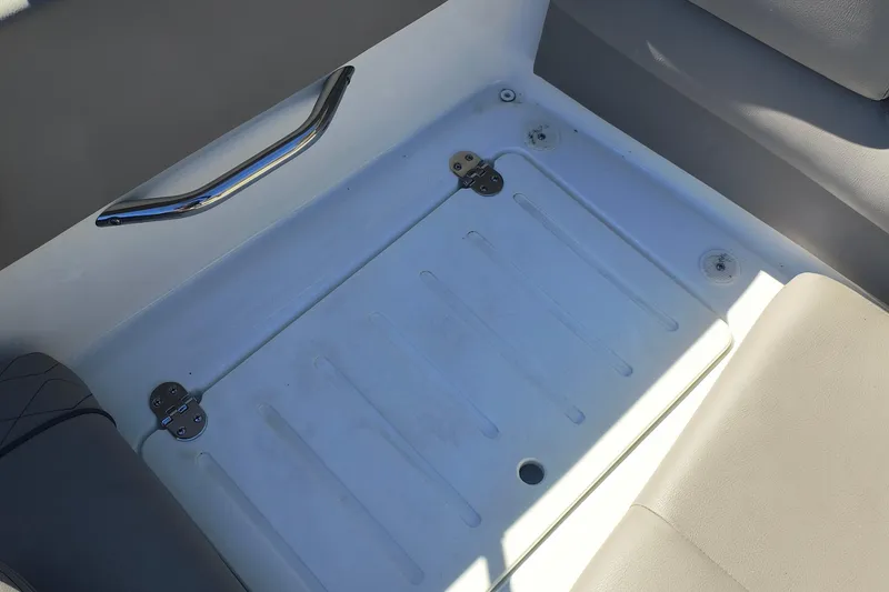 Slide: The Image of 2024 Glastron GX 215 boat interior storage compartment with metal handle and cushioned seating. - 21