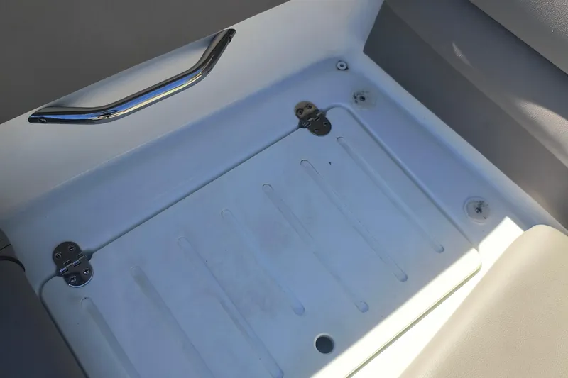 Slide: The Image of 2024 Glastron GX 215 boat storage compartment with metal handle and hinges. - 22