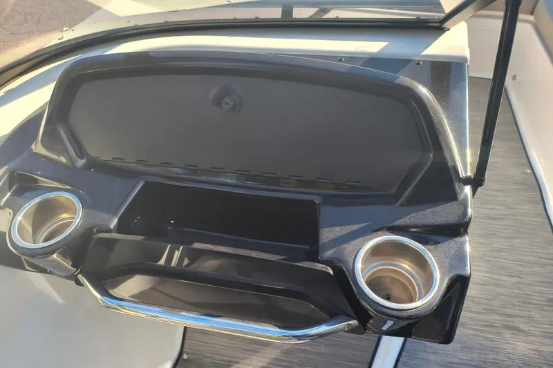 Slide: The Image of 2024 Glastron GX 215 boat dashboard with open storage compartment and cup holders. - 5