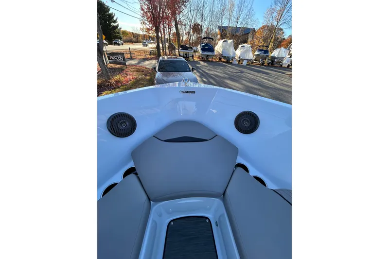 Slide: The Image of 2024 Glastron GX 215 boat interior with gray seating and speakers, parked outdoors. - 50