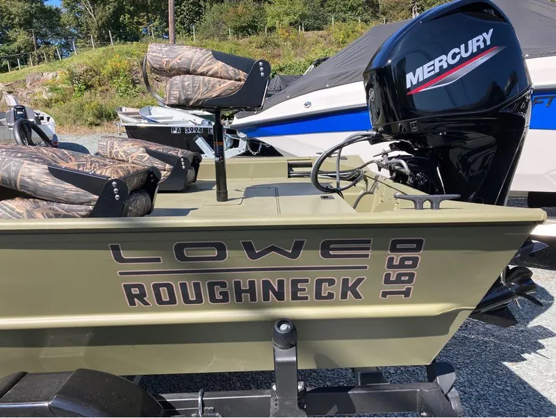 Slide: The Image of 2024 Lowe Roughneck RX1660 SC boat with Mercury engine, camo seats, parked outdoors. - 2