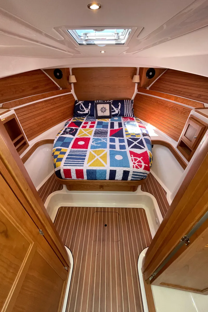 Slide: The Image of 2024 Back Cove 34O cabin interior with nautical-themed bedding and wood paneling. - 41