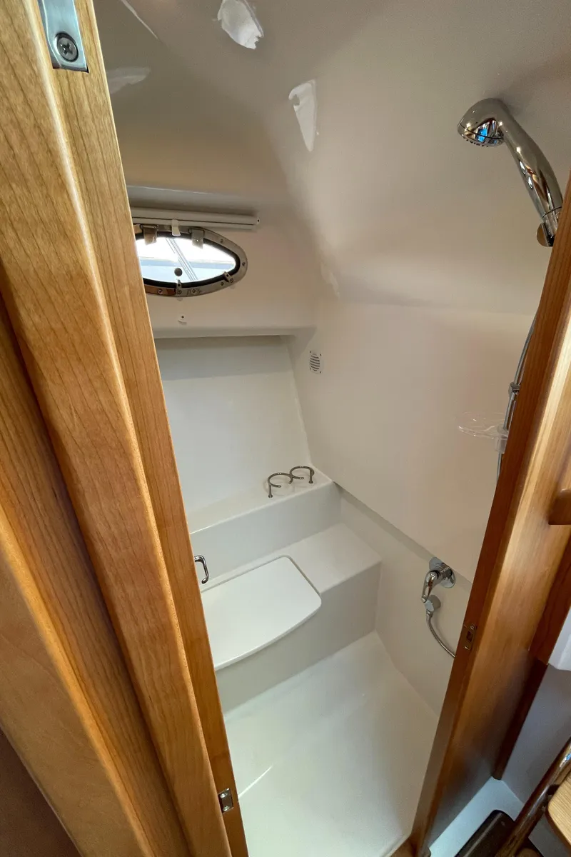 Slide: The Image of 2024 Back Cove 34O boat bathroom with shower, wooden door, and porthole window. - 49
