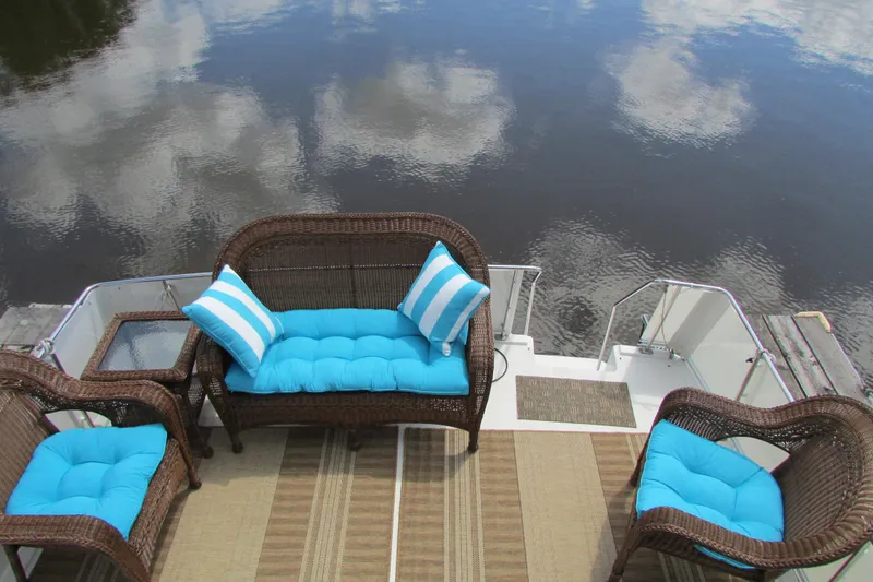 Slide: The Image of 1995 Carver 325 Aft Cabin with wicker seating and blue cushions on a serene water backdrop. - 4
