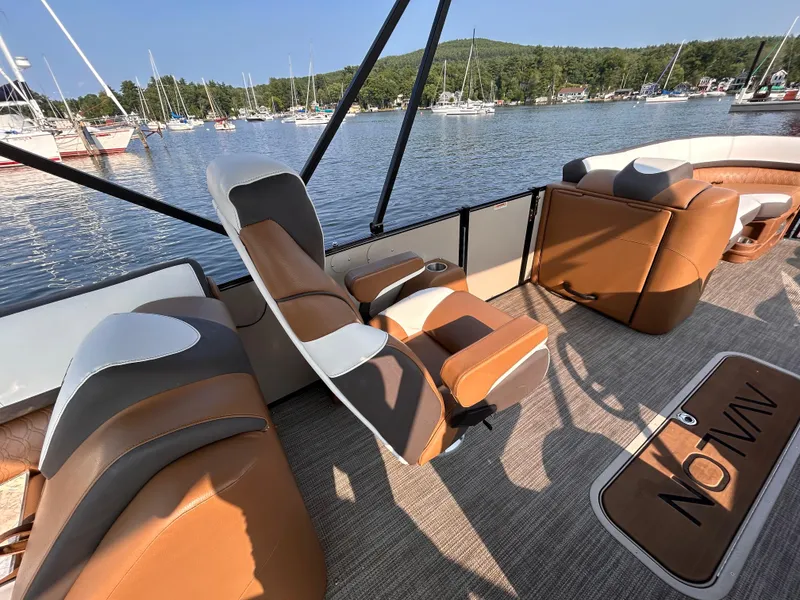 Slide: The Image of 2024 Avalon Catalina Quad Lounge boat interior with brown seating, docked by a scenic lake. - 29